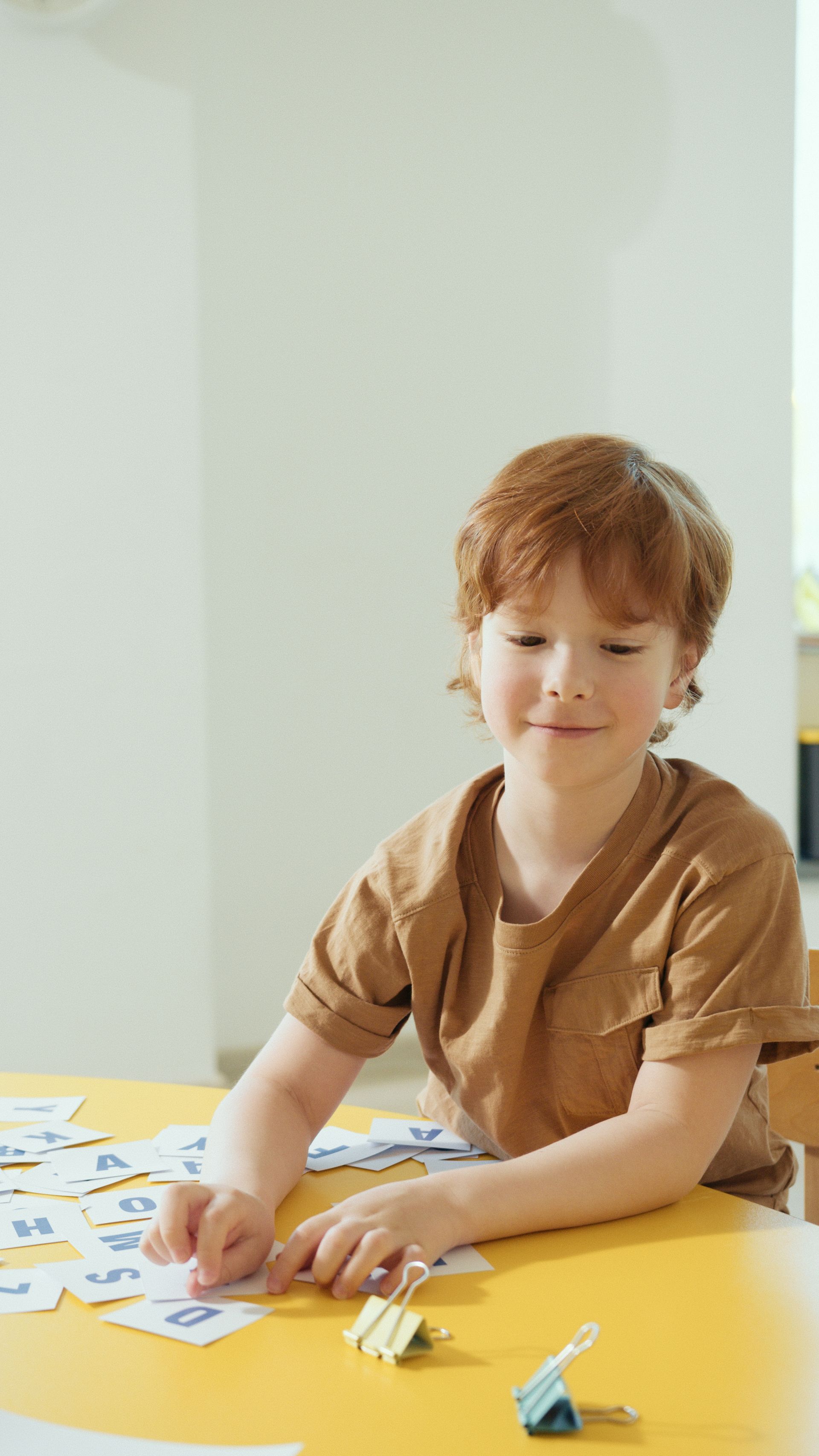 A young boy works with letter cards at a bright yellow table in a clinic classroom