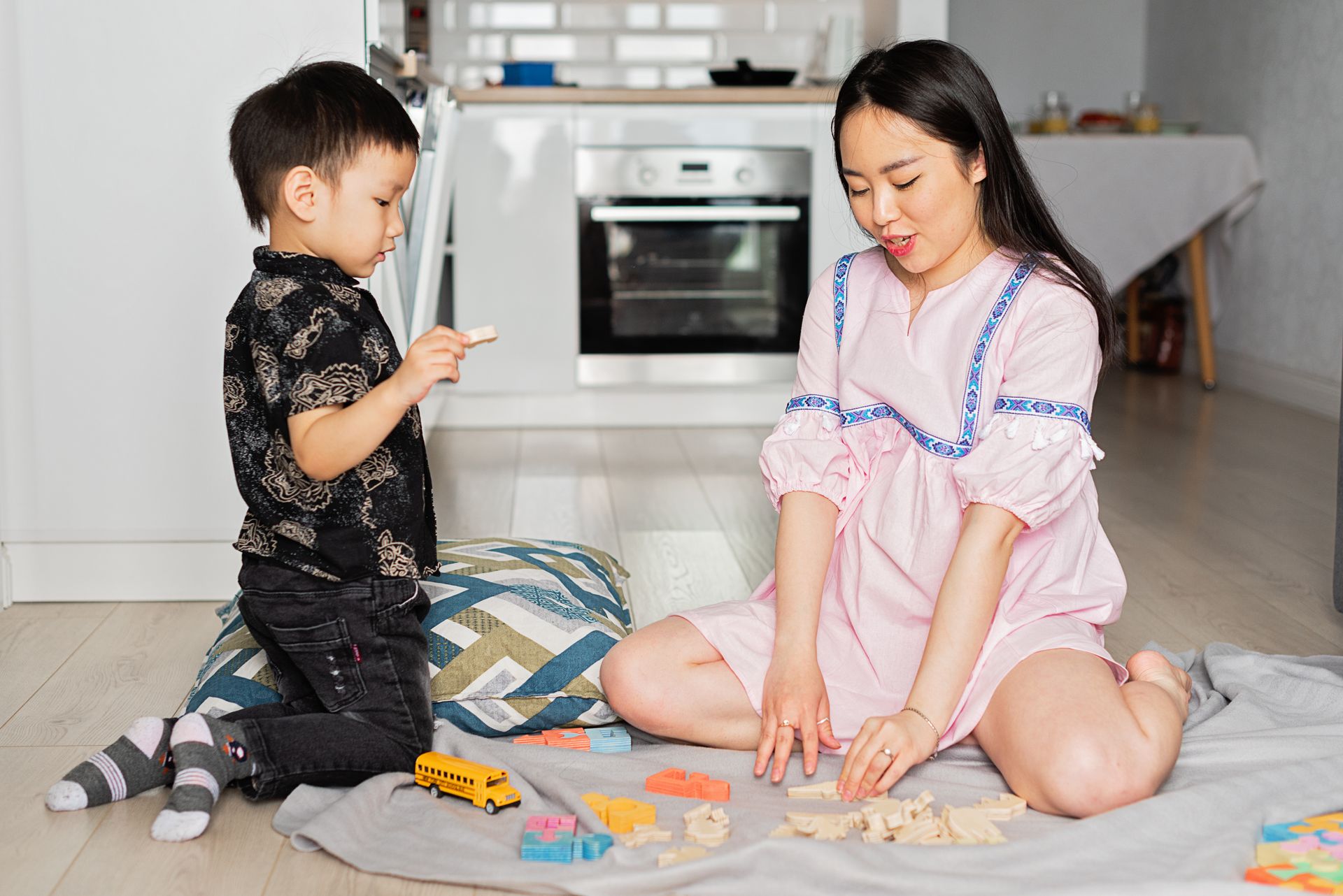 A mother and her young son build with colorful blocks together in a bright kitchen