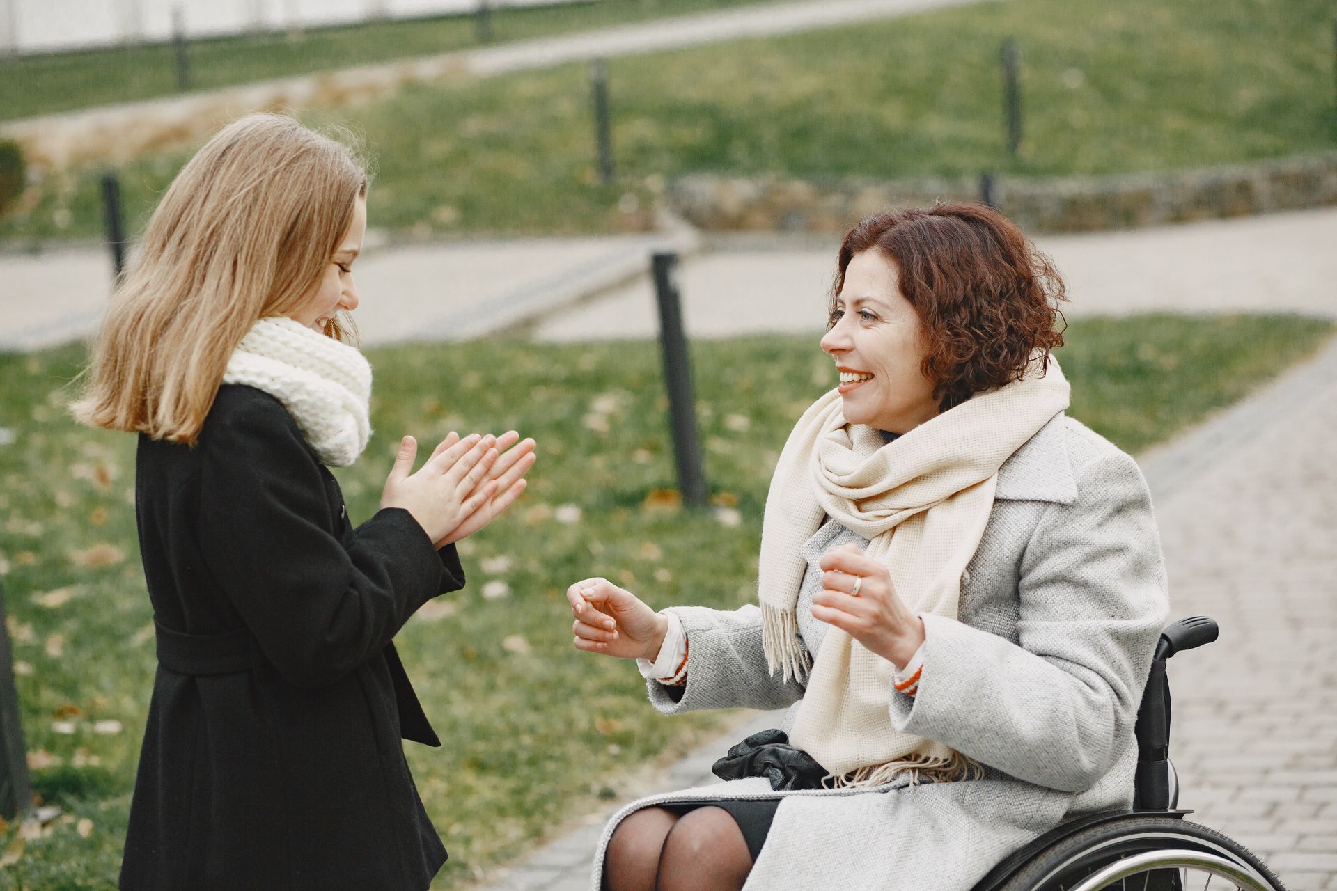 A woman in a wheelchair plays a clapping game with a young girl at the park