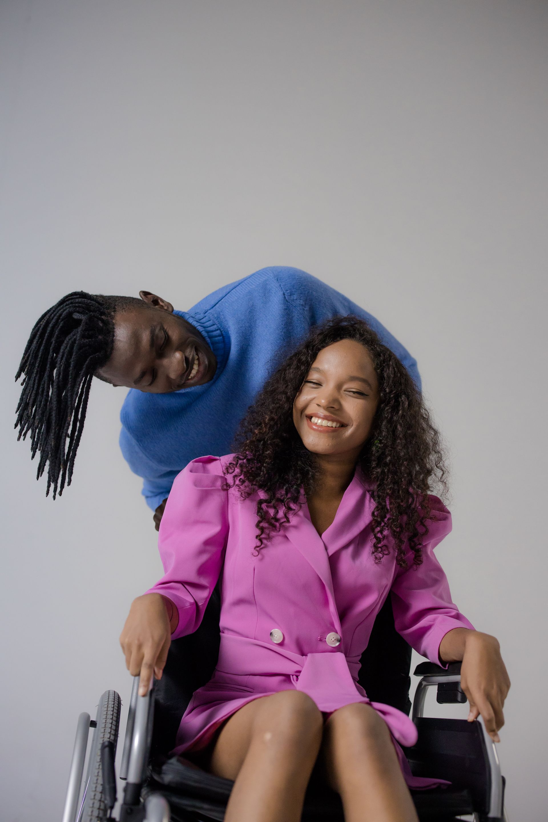 A man leans in laughing with a joyful young woman seated in her wheelchair