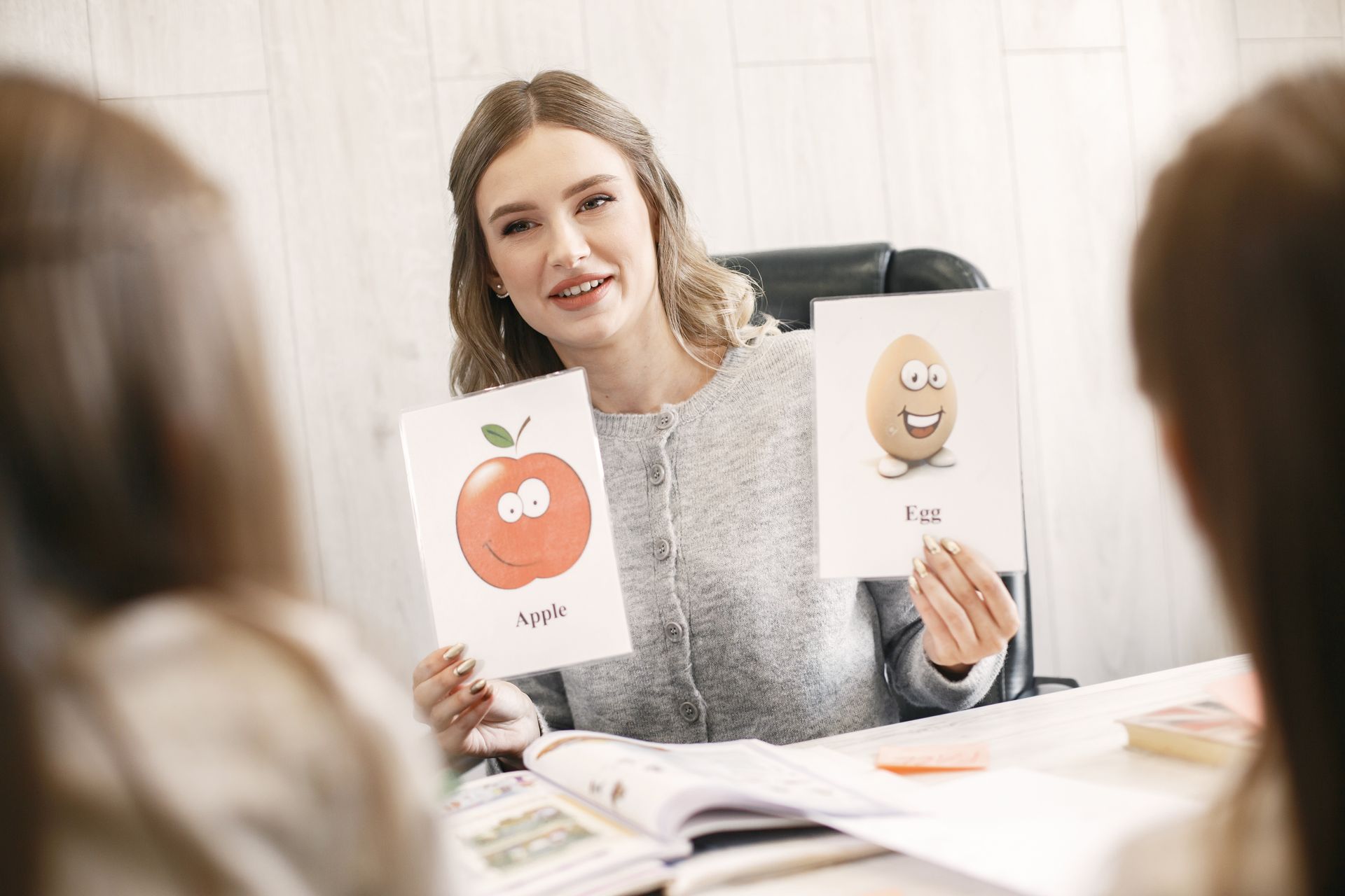 A speech therapist holds up apple and egg picture cards for two children across the table